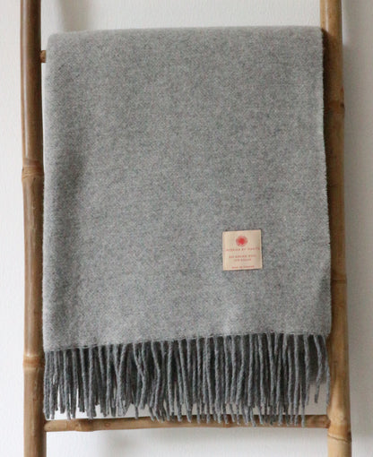 Graue Merino Wolle Tagesdecke 140x200 cm von Interior by Hakito, weich und atmungsaktiv, dekorativ angeordnet auf einer Leiter.