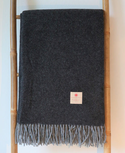 Dunkelgraue Merino Wolle Tagesdecke 140x200 cm von Interior by Hakito, dekorativ angeordnet auf einer Leiter mit Fransen.