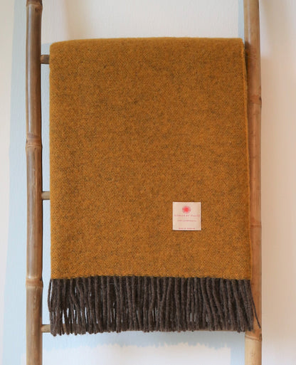 Robuste Lammwolle Tagesdecke von Interior by Hakito in warmem Gelb, hängend an einer Leiter, ideal für gemütliche Abende.