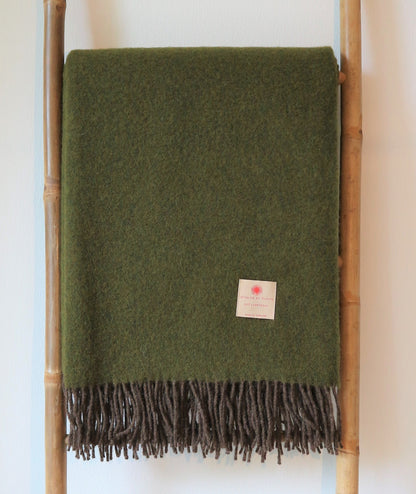 Geeignetes Bild einer robusten Lammwolle Tagesdecke von Interior by Hakito, in olivgrün, dekorativ auf einem Holzständer präsentiert, perfekt für warme Abende.