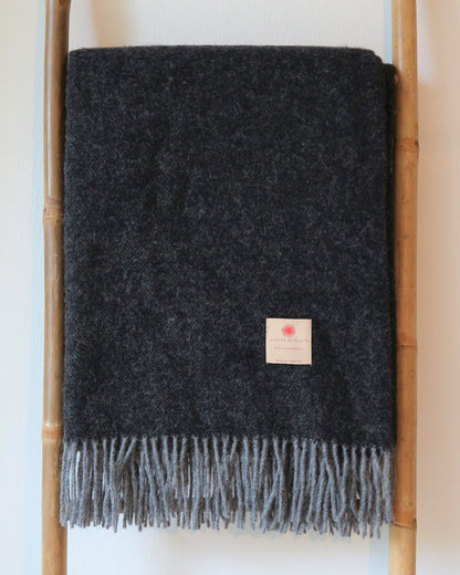 Schicke Robuste Lammwolle Tagesdecke von Interior by Hakito in dunklem Farbton, stilvoll gefaltet über einem Holzregal.