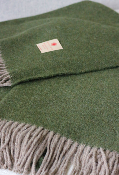 Warme Merino Wolle Tagesdecke von Interior by Hakito in einem sanften Olivgrün mit weichen Fransen, ideal für den Komfort in Ihrem Zuhause.