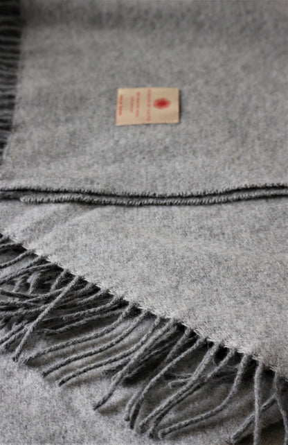 Detailansicht der Fransen der grauen Merino Wolle Tagesdecke 140x200 cm von Interior by Hakito, mit Etikett.