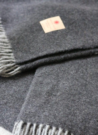 Warme Merino Wolle Tagesdecke von Interior by Hakito, in dunklem Grau mit Etikett, ideal für ein gemütliches Zuhause.