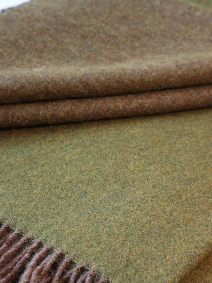 Nahaufnahme einer olivgrünen robusten Lammwolle Tagesdecke von Interior by Hakito, gefaltet, weich und einladend, ideal für Entspannung.