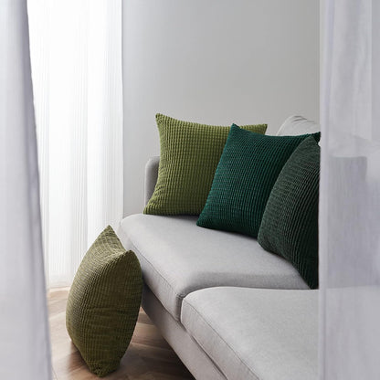 Grüne Kissen in verschiedenen Größen auf einem grauen Sofa, Modell Sven Kordsamt von Interior by Hakito, schaffen einladenden Komfort.